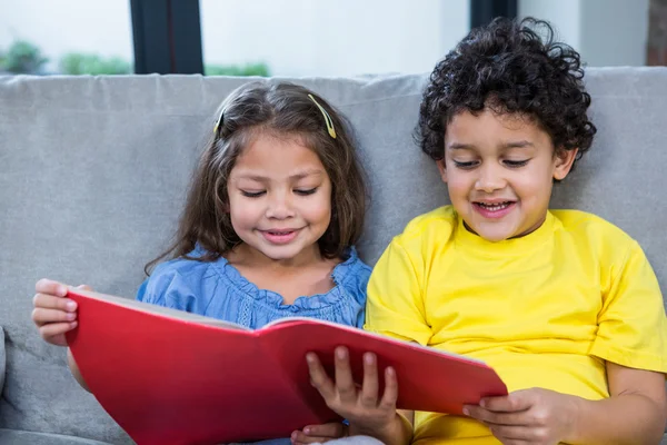 Söta syskon läser en bok i soffan — Stockfoto