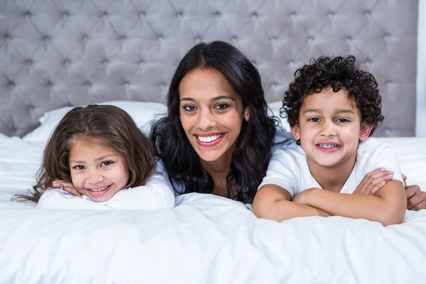 Улыбающаяся мать с детьми на кровати — стоковое фото
