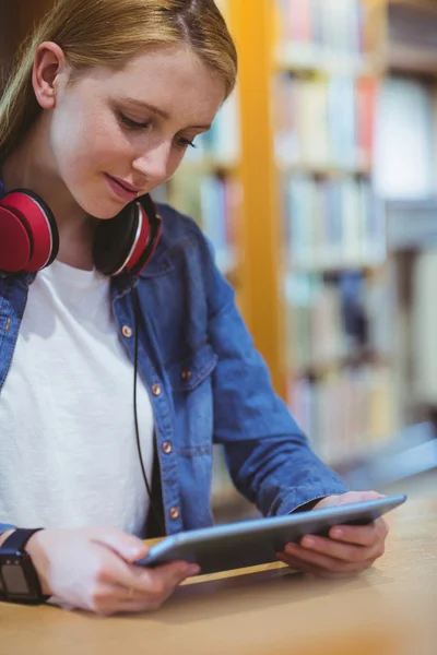 Pretty student with headphones using tablet in library — Stock Photo, Image