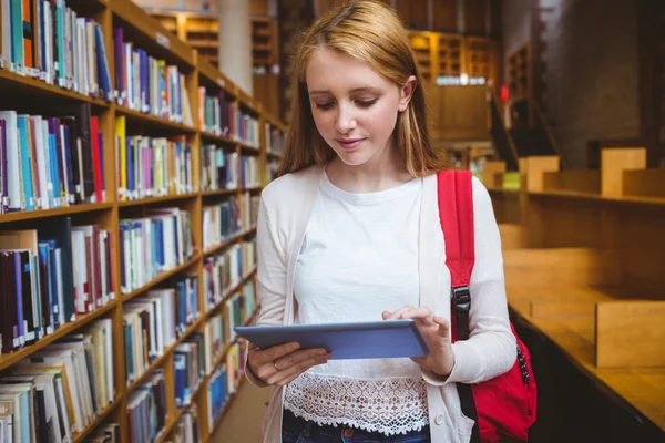 Estudiante rubio con mochila usando tableta en la biblioteca —  Fotos de Stock