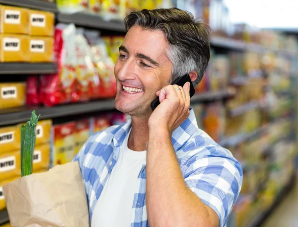 Homme souriant lors d'un appel téléphonique avec sac d'épicerie — Photo