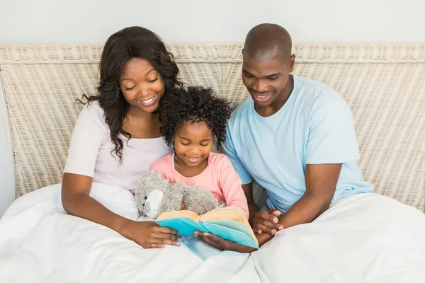 Pretty couple with her daughter reading a book in bed — Stock Photo, Image