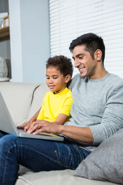 Sorrindo pai e filho usando laptop no sofá — Fotografia de Stock