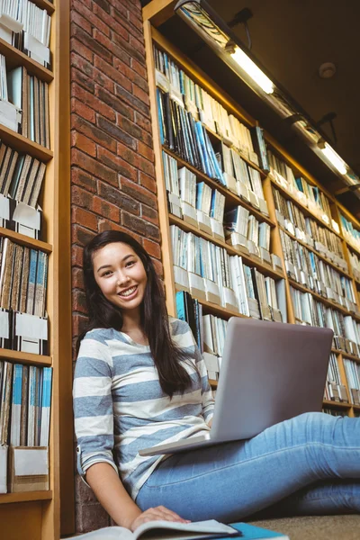 Estudiante sonriente sentado en el suelo contra la pared en la biblioteca stu —  Fotos de Stock