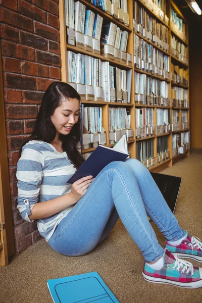 Smiling student sitting on the floor against wall in library rea Stock Photo