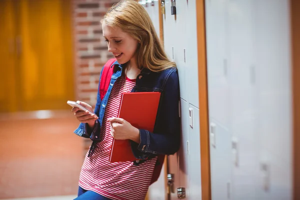 Lachende student leunend tegen de locker gebruikend smartphone — Stockfoto