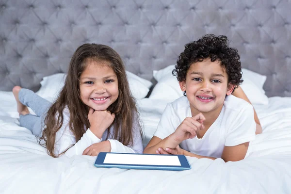 Söta syskon med tablett på sängen — Stockfoto