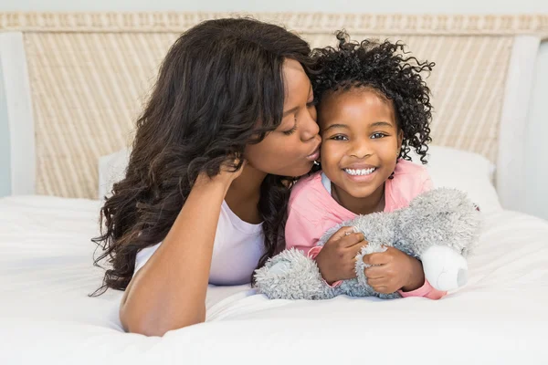 Moeder haar lachende dochter kussen op bed — Stockfoto