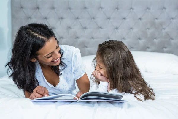 Happy mother and daughter reading a book on the bed — Stock Photo, Image