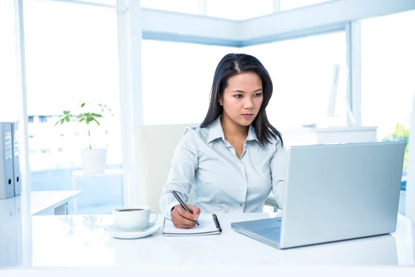 Mujer de negocios seria escribiendo en el bloc de notas y utilizando el ordenador portátil — Foto de Stock