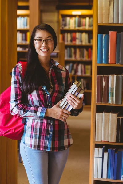 Estudante sorrindo segurando livros na biblioteca — Fotografia de Stock