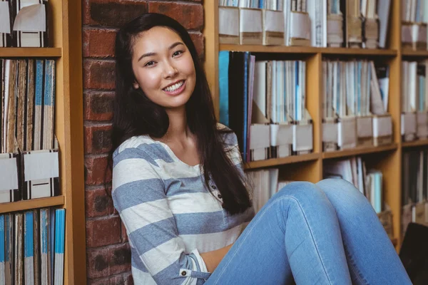 Lachende student zittend op de vloer tegen muur in bibliotheek — Stockfoto