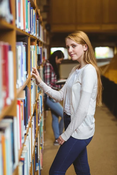 Blond student op zoek naar boek in de bibliotheek planken — Stockfoto