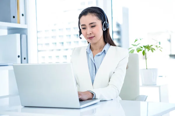 Donna d'affari sorridente con auricolare utilizzando il computer portatile — Foto Stock