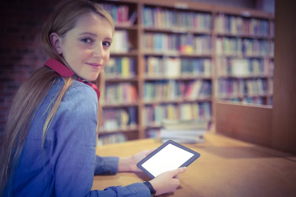 Estudante bonito com fones de ouvido usando tablet na biblioteca — Fotografia de Stock