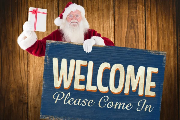 Santa shows a present while holding sign — Stock Photo, Image