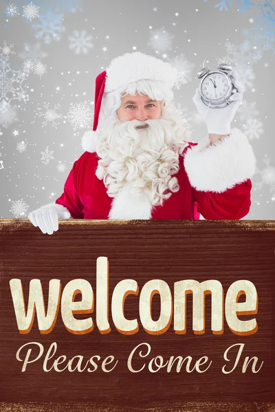 Composite image of santa claus holding alarm clock and sign — Stock Photo, Image