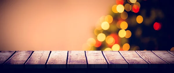 Wooden desk against christmas tree — Stock Photo, Image