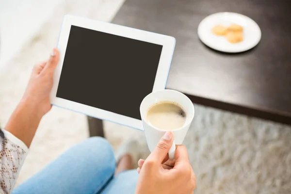 Mujer casual sonriente usando su tableta mientras sostiene el café — Foto de Stock