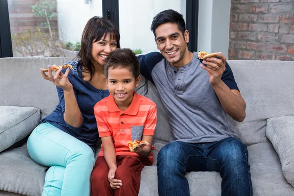 Famille souriante mangeant de la pizza sur le canapé — Photo