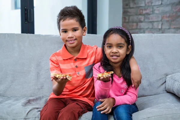 Lächelnde Geschwister beim Pizza essen auf dem Sofa — Stockfoto