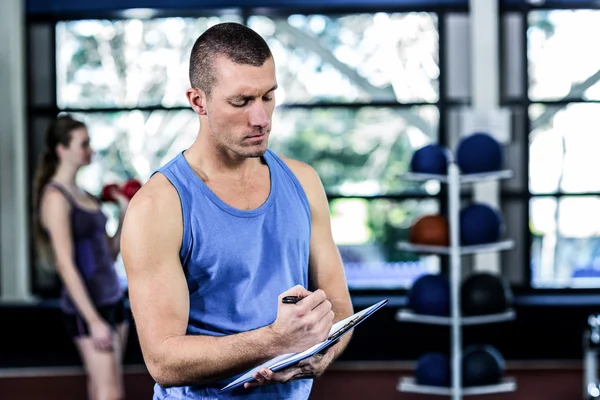 Muscular trainer writing on clipboard — Stok Foto