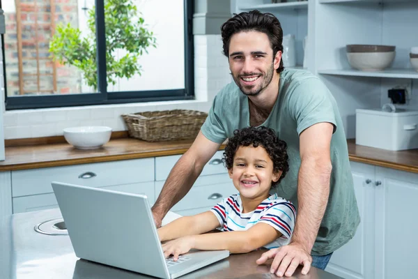 Sorrindo pai usando laptop com seu filho na cozinha — Fotografia de Stock