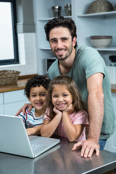 Smiling father using laptop with his children in kitchen — Stock Photo, Image