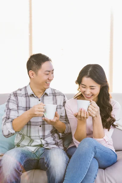 Lyckliga paret håller kaffekoppen när man sitter på soffan — Stockfoto