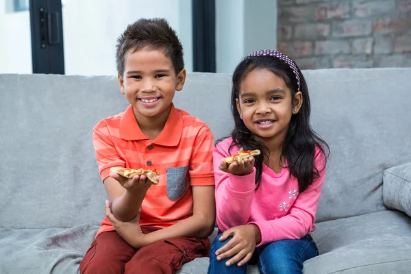 Sorridenti fratelli che mangiano pizza sul divano — Foto Stock