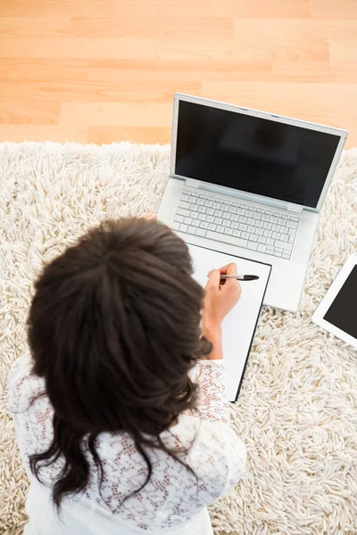 Woman writing note while using her laptop — Stock Photo, Image