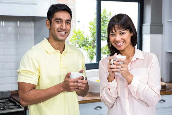 Pareja feliz sonriendo a la cámara mientras sostiene tazas —  Fotos de Stock