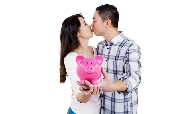 Casal beijando enquanto segurando porquinho banco — Fotografia de Stock