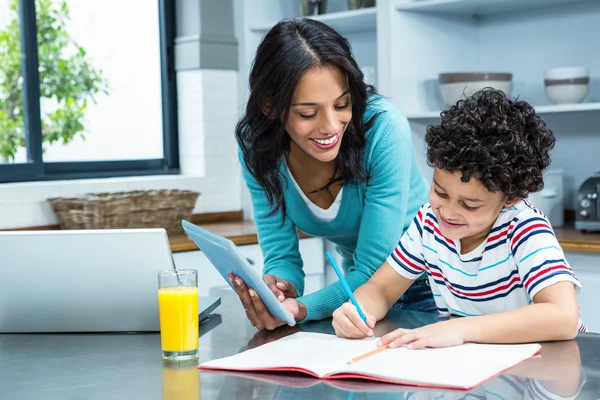 Kind mother helping her son doing homework in kitchen