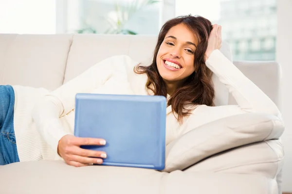 Mulher sorrindo usando seu tablet no sofá — Fotografia de Stock