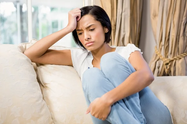 Frowning brunette sitting on the sofa — Stock Photo, Image