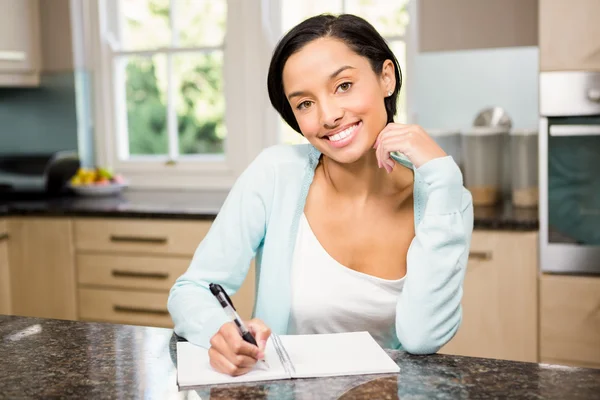 Uśmiechnięta brunetka pisania na skrypt dłużny podkładka — Zdjęcie stockowe