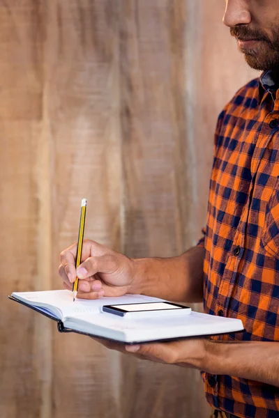 Geschäftsmann mit Smartphone schreibt auf Buch — Stockfoto