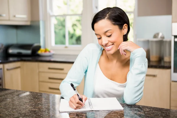 Sonriente morena escribiendo en bloc de notas — Foto de Stock