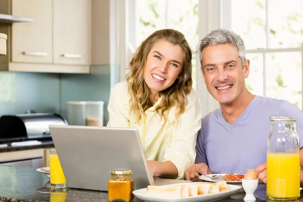 Pareja usando el ordenador portátil y desayunando —  Fotos de Stock