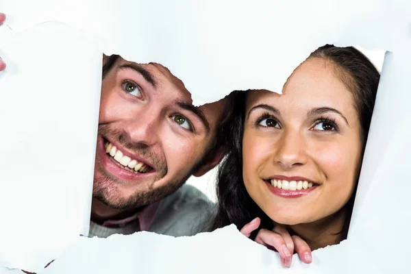 Sorrindo casal espreitando papel rasgado — Fotografia de Stock