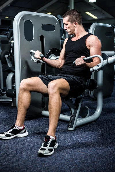 Muscular man using exercise machine — Stock Photo, Image