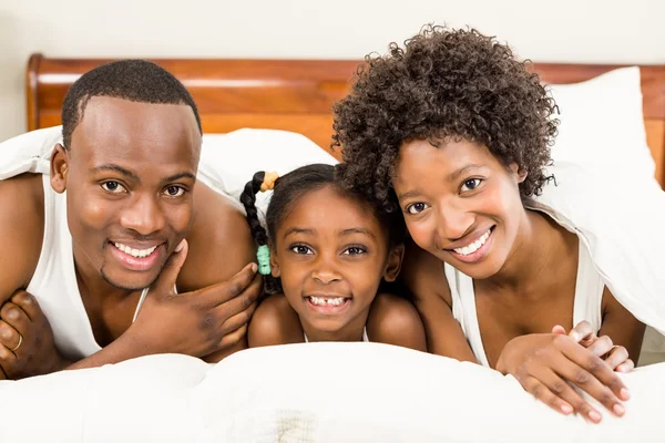 Família sorridente deitada na cama — Fotografia de Stock