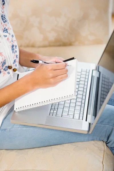 Femme écrit sur un bloc-notes avec ordinateur portable — Photo