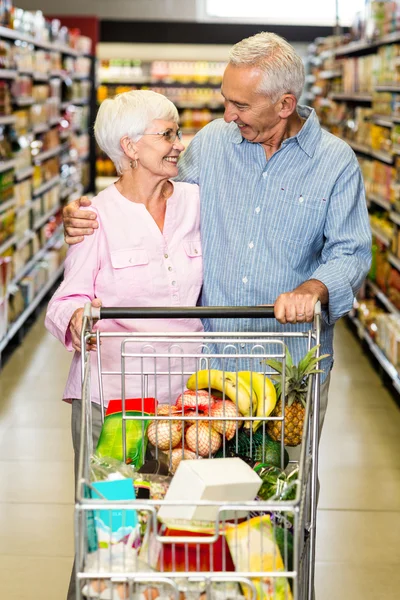 Senior couple embracing while pushing cart — Stock Photo, Image
