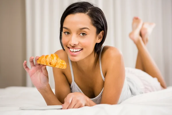 Smiling brunette eating croissant — Stock Photo, Image