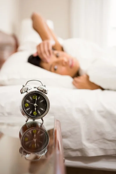 Alarm clock against brunette on bed — Stock Photo, Image