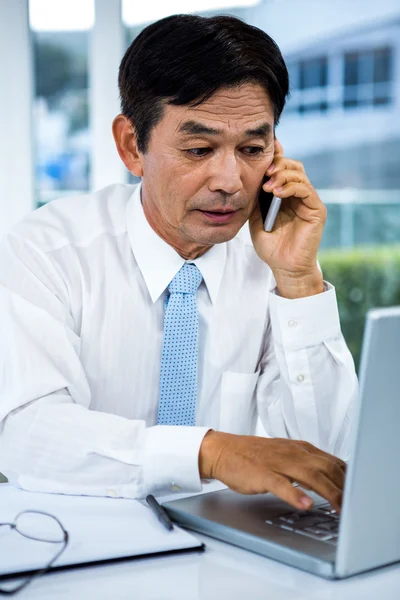 Aziatische zakenman aan de telefoon met behulp van zijn computer — Stockfoto