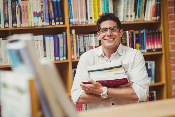 Lachende nerd houdt van boeken in bibliotheek — Stockfoto