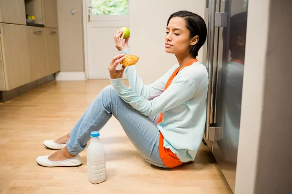 Morena inquieta sosteniendo manzana y postre —  Fotos de Stock